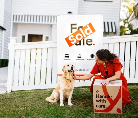 Golden retriever sitting in front of sold house sign