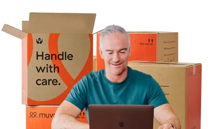 Older man finding removalists on laptop with moving boxes behind him