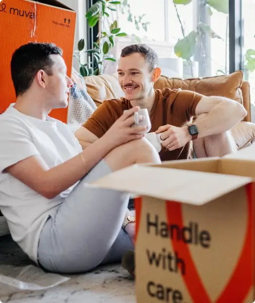 Two guys sitting on the floor of their apartment with Muval moving boxes
